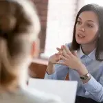 Due persone sedute a un tavolo in un ambiente d’ufficio durante un incontro professionale, con una persona che tiene documenti tra le mani, a rappresentare un colloquio o una valutazione legata alle assunzioni agevolate di lavoratrici svantaggiate