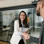 Due persone in un ambiente d’ufficio si stringono la mano durante un incontro professionale, mentre una di esse tiene documenti tra le mani, a rappresentare accordi e procedure legate alle assunzioni agevolate di giovani lavoratori.