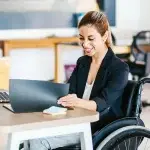 Persona seduta alla scrivania in un ambiente d’ufficio mentre consulta dei documenti, con un computer portatile e materiale di lavoro sul tavolo, a rappresentare attività amministrative e processi legati all’assunzione di lavoratori con disabilità.