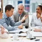 Persone sedute attorno a un tavolo in un ufficio, impegnate in una riunione con documenti e tablet appoggiati sul piano di lavoro, a rappresentare attività di analisi e gestione degli incentivi per l’assunzione di lavoratori over 50.