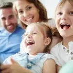 Persone sedute vicine su un divano in un ambiente domestico, tra cui un bambino in primo piano, a rappresentare un contesto familiare legato ai sostegni economici per i nuclei con figli.