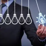 Persona in abbigliamento professionale che tocca un’icona digitale a forma di lampadina con il simbolo del denaro, mentre una serie di altre lampadine stilizzate è allineata di fronte, a rappresentare misure economiche, incentivi e strategie di sostegno alle imprese.
