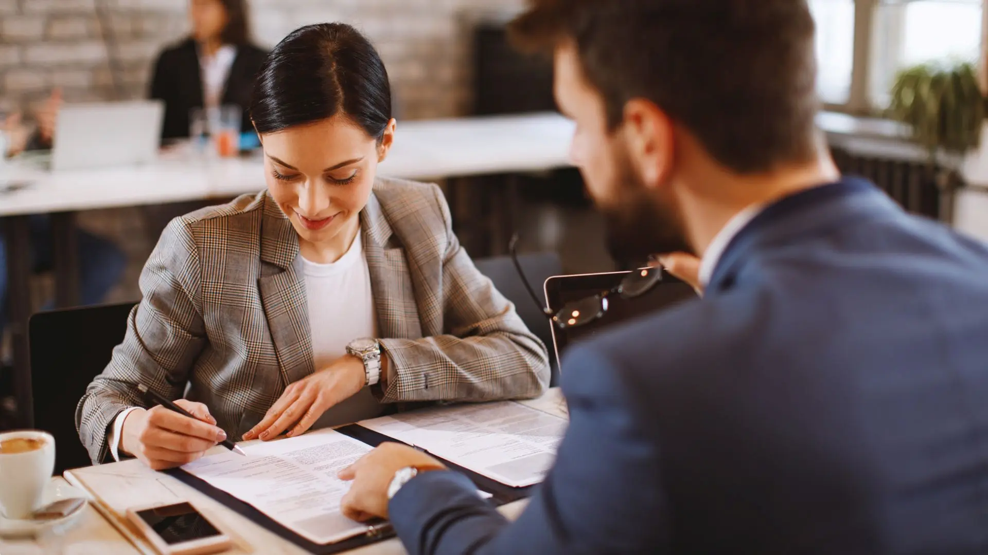 Due persone sedute a un tavolo in un ambiente d’ufficio mentre esaminano documenti e compilano moduli, con quaderni e strumenti di lavoro sul tavolo, a rappresentare attività amministrative e procedure legate alla formazione finanziata dal Fondo Nuove Competenze.