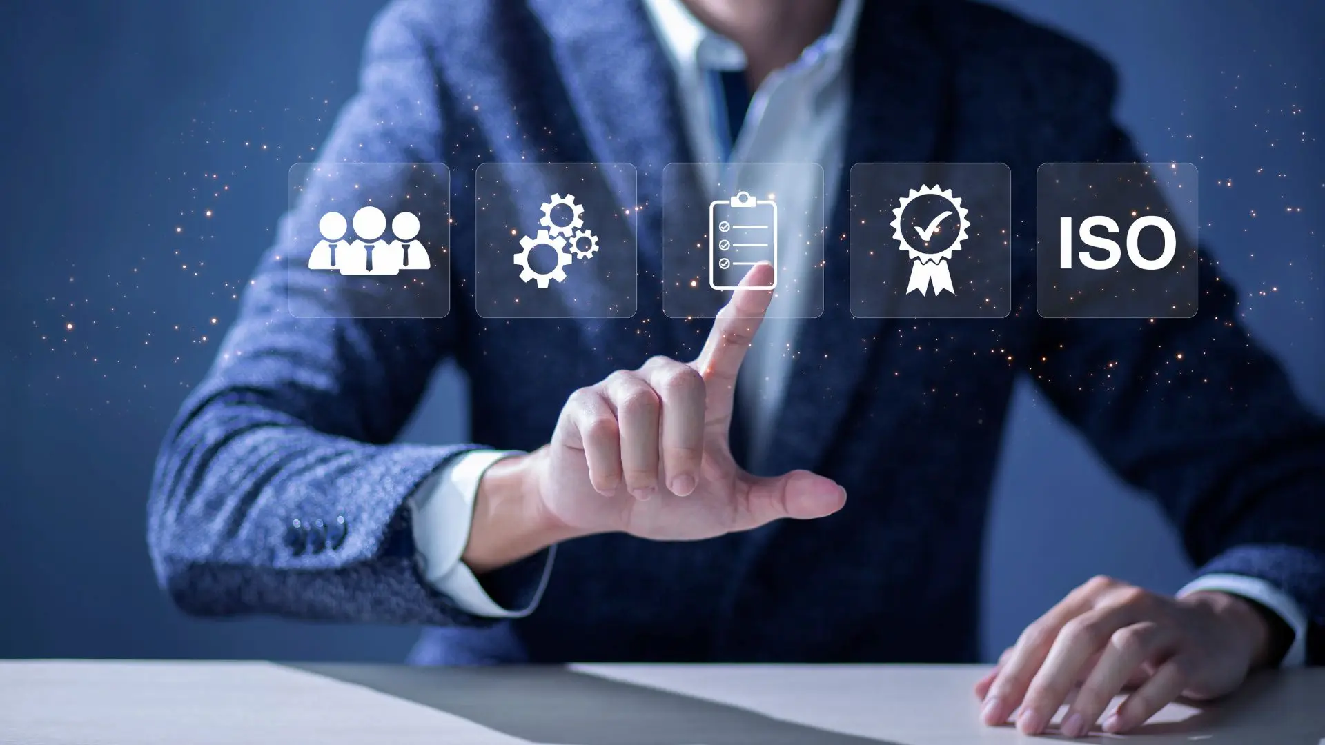 Persona seduta a un tavolo che seleziona icone digitali sospese rappresentanti un team, ingranaggi, una checklist e un simbolo di certificazione, con la parola “ISO” visibile a destra, a indicare concetti di qualità, conformità e sistemi di gestione.