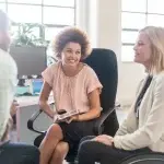 Tre persone sedute attorno a un tavolo in un ufficio luminoso, impegnate in un confronto professionale, con una delle persone seduta su una sedia ergonomica dotata di rotelle, a rappresentare un contesto di inclusione lavorativa e dialogo strutturato.
