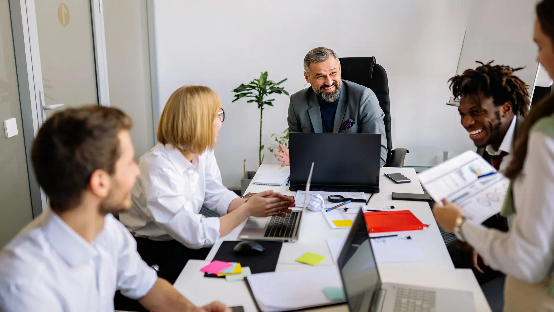 Persone sedute attorno a un tavolo in un ufficio moderno durante una riunione, con laptop, documenti e appunti sul tavolo, a rappresentare attività di analisi HR e processi organizzativi legati alla trasparenza retributiva.