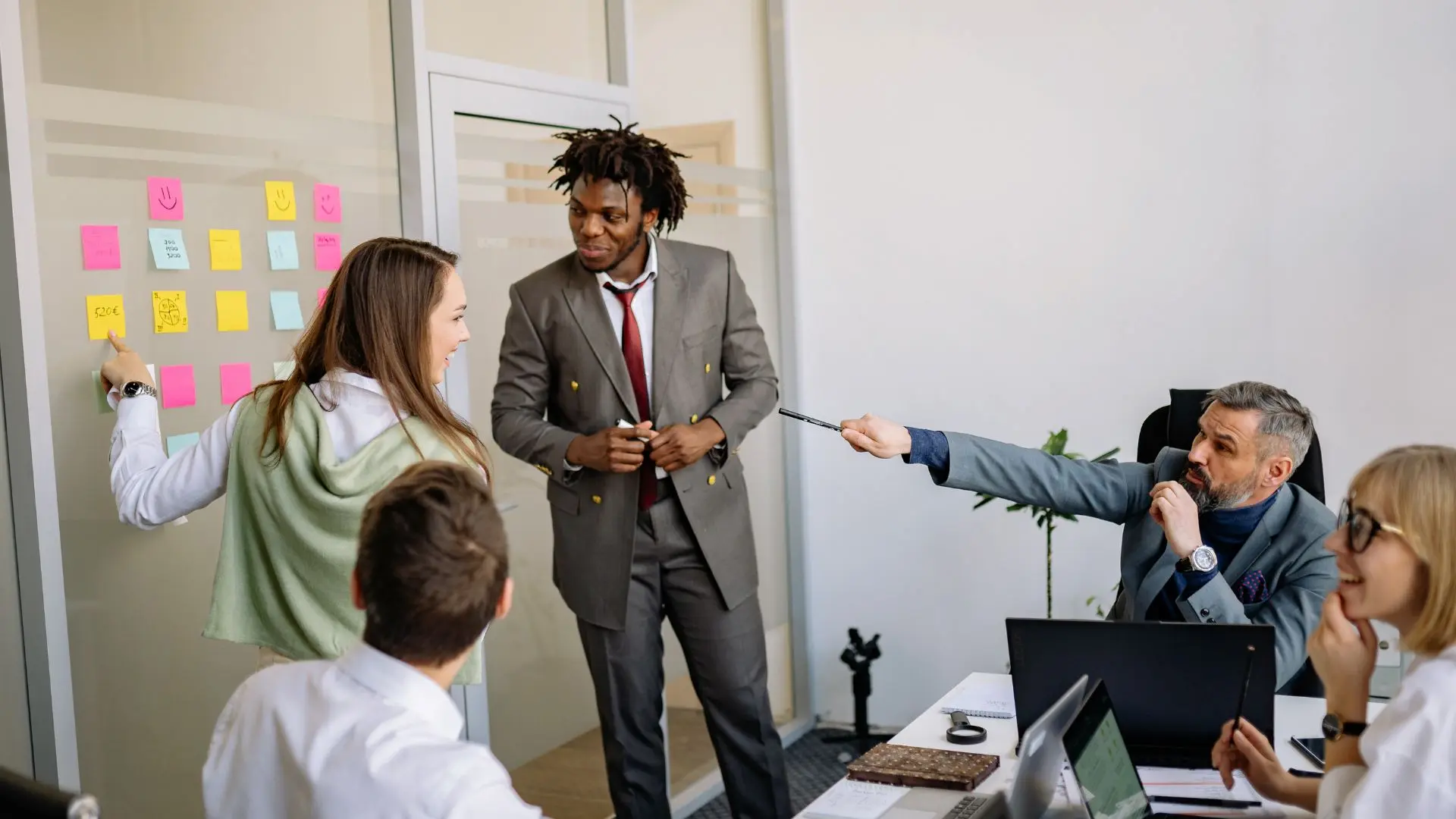 Persone riunite in un ufficio attorno a un tavolo, mentre collaborano utilizzando laptop, documenti e una lavagna con post‑it, a rappresentare attività organizzative e interventi migliorativi in ambito sicurezza sul lavoro.