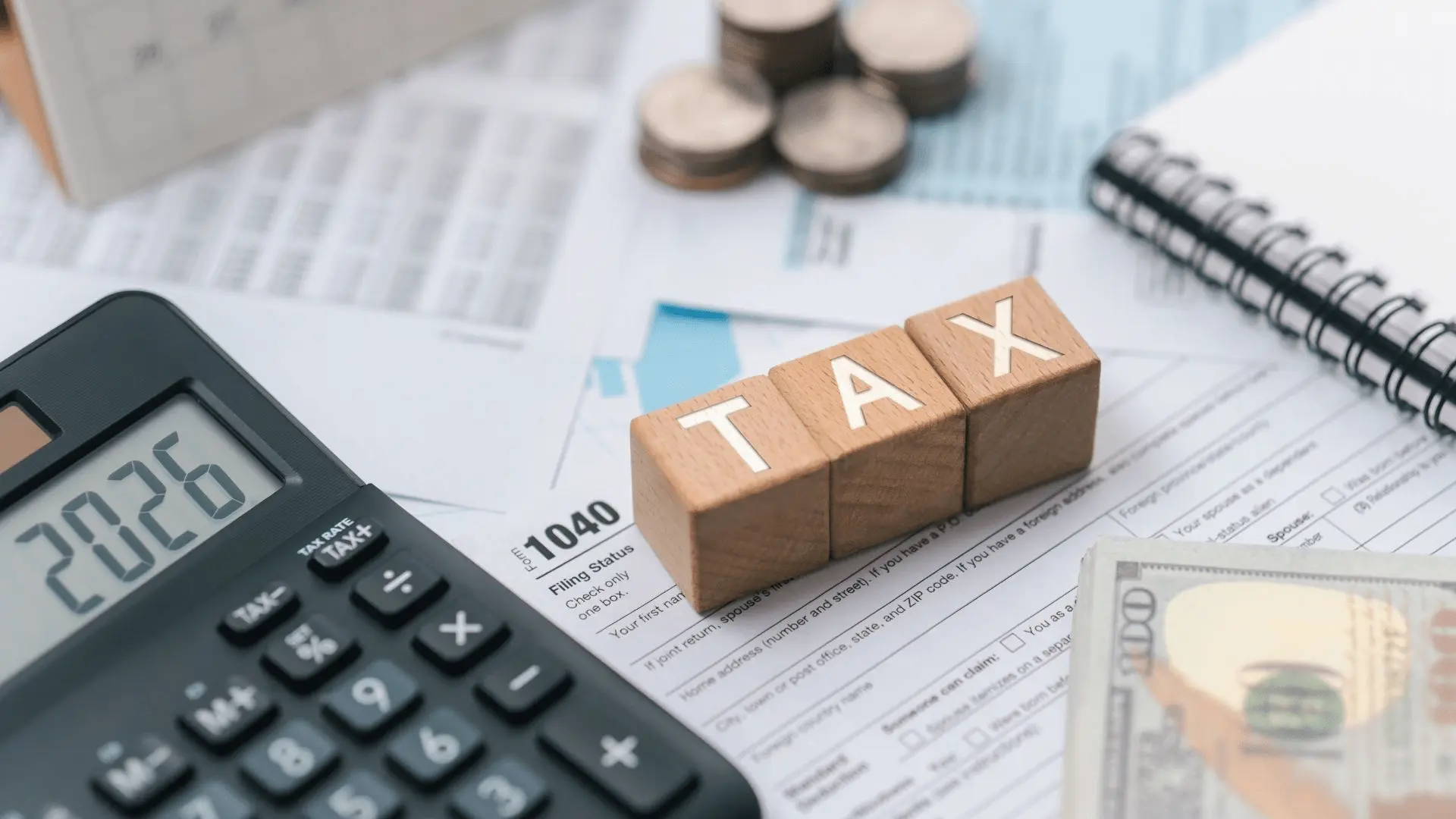 Scrivania con calcolatrice, documenti fiscali, monete, banconote e cubi di legno con la scritta “TAX”, a rappresentare agevolazioni contributive e misure fiscali per le imprese.