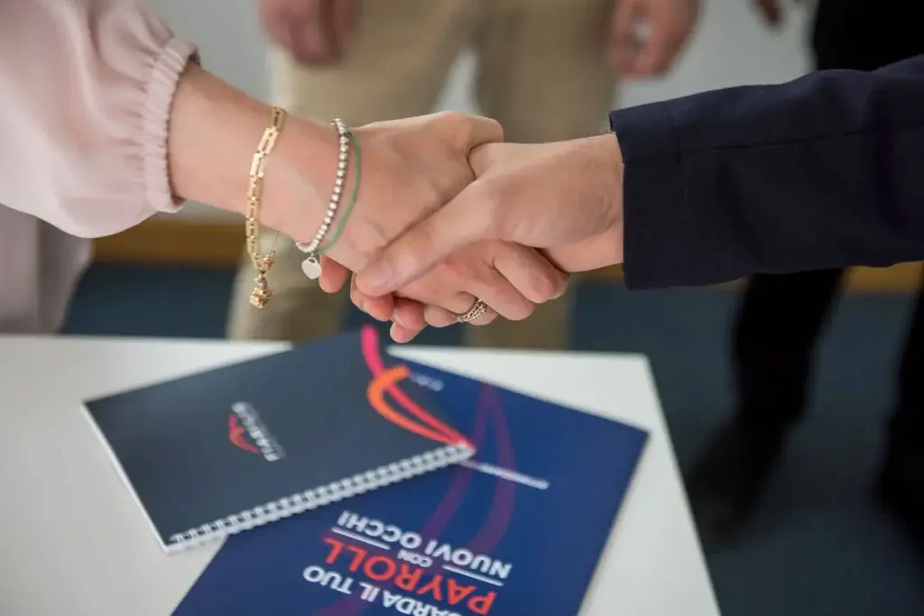 Stretta di mano tra due persone in un contesto professionale, con documenti e materiale informativo appoggiati sul tavolo recanti il logo Fiabilis, a rappresentare la formalizzazione di accordi o assunzioni legate all’esonero contributivo ADI/SFL.