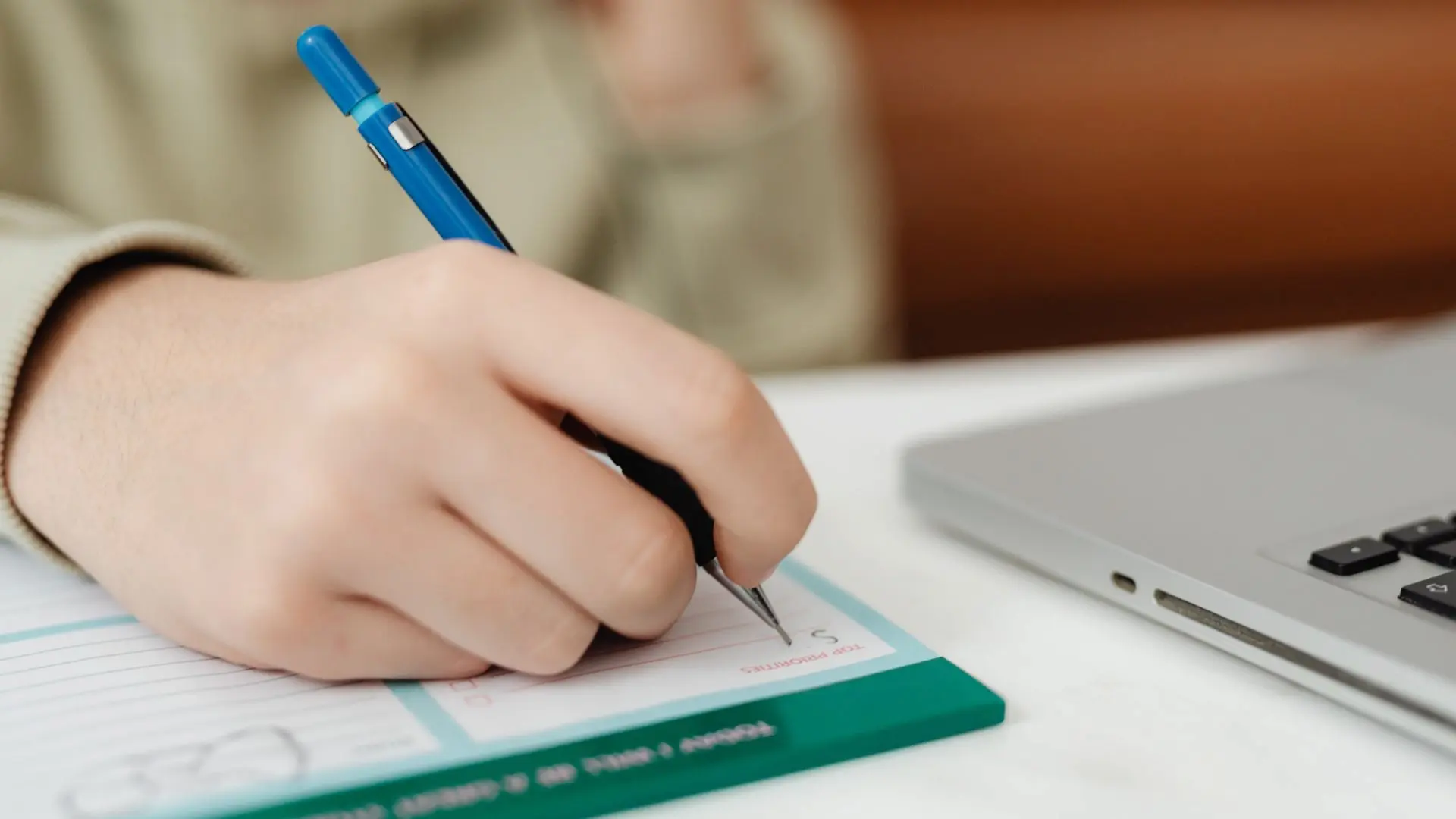 Mano che compila un modulo cartaceo con una penna accanto a un computer portatile, a rappresentare la richiesta di incentivi o la gestione amministrativa di procedure legate alle assunzioni e alla formazione.