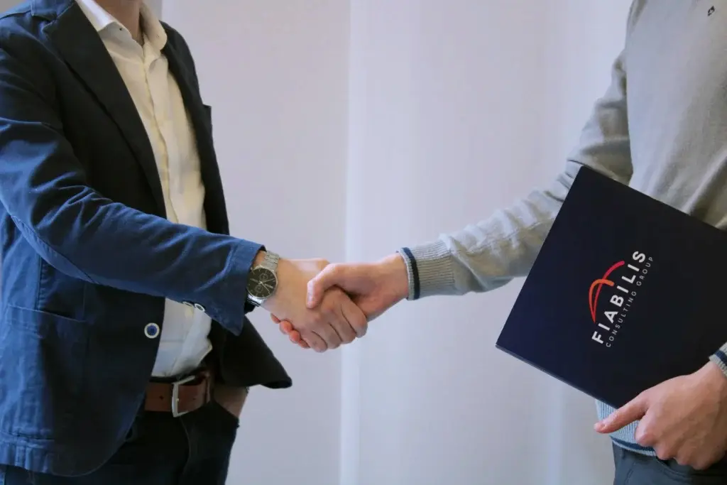 Due persone che si stringono la mano in un contesto professionale, una delle quali tiene una cartellina con il logo Fiabilis, a rappresentare accordi e procedure legate alle assunzioni incentivate di lavoratori con disabilità.