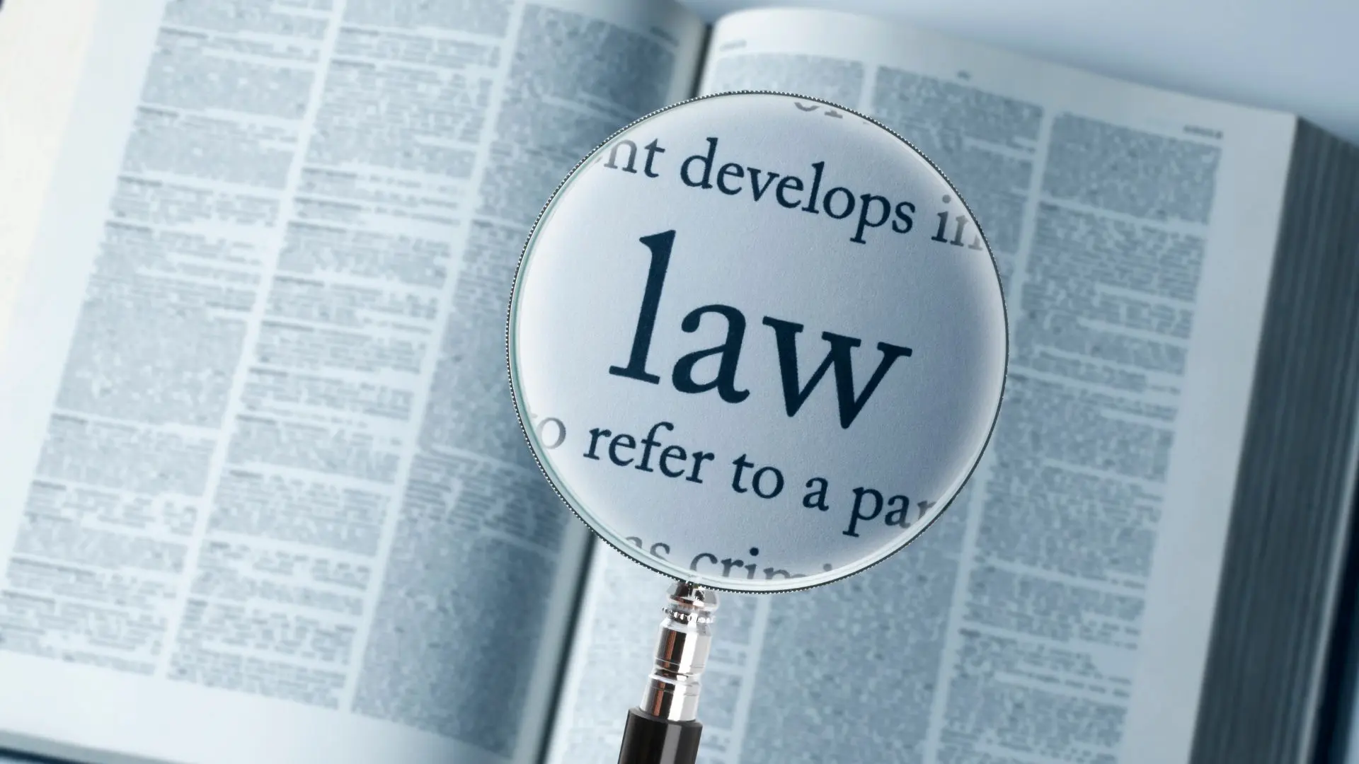 Lente d’ingrandimento posata su una pagina aperta di un libro di testo giuridico, con la parola “law” ingrandita al centro, a rappresentare analisi normativa e approfondimento legislativo.