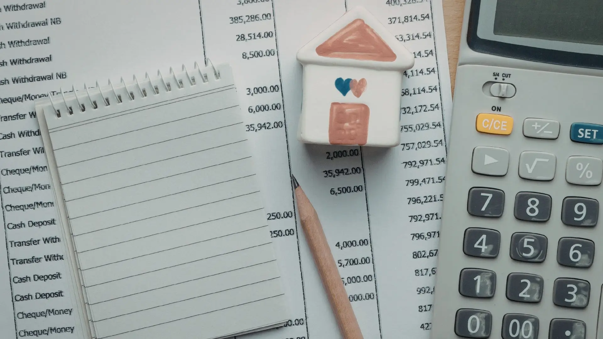 Calcolatrice, fogli con importi e movimenti contabili, taccuino e una piccola casa decorativa su una scrivania, a rappresentare calcoli e verifiche legate alla riduzione contributiva nel settore edilizio.