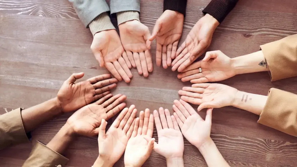 Una serie di mani aperte disposte in cerchio sopra un tavolo in legno, a rappresentare inclusione, supporto reciproco e collaborazione in un contesto collettivo.