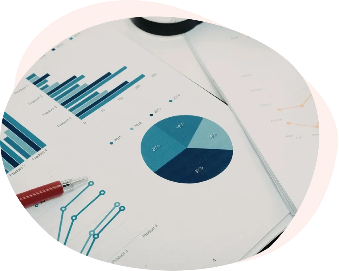 Documenti cartacei stampati contenenti report finanziari, grafici a barre, a torta e a linee appoggiati su una scrivania. Sopra i fogli sono presenti una penna rossa, una lente d'ingrandimento e un paio di occhiali da vista con montatura nera. L'immagine rappresenta l'attività di studio approfondito, data mining e business intelligence necessaria per analizzare e ottimizzare il costo del lavoro.