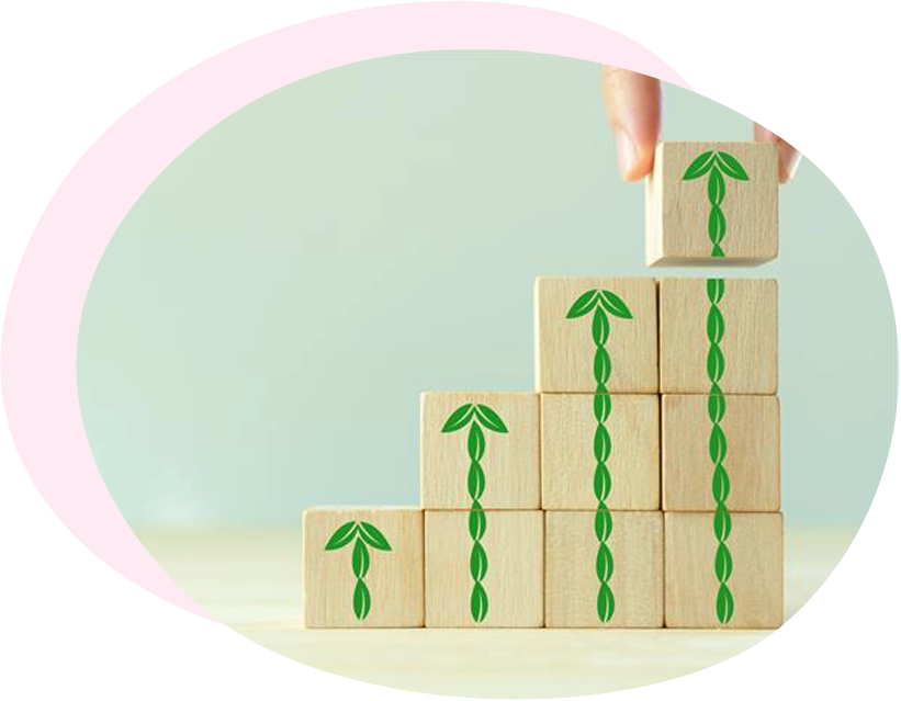 Dettaglio di una mano che posiziona l'ultimo blocco di legno in cima a una pila a forma di scala, con motivi a viticci e frecce verdi a spirale che si collegano per mostrare una crescita ESG continua. Lo sfondo è verde salvia con un accento rosa sfumato.