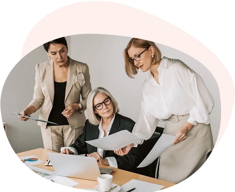 Tre professioniste mature riunite attorno a una scrivania in un ufficio luminoso, intente ad analizzare documenti finanziari, grafici a torta e dati su un computer portatile. L'immagine rappresenta il servizio di consulenza su misura, l'analisi delle posizioni contributive e il Longevity Planning per costruire un futuro previdenziale solido e consapevole.