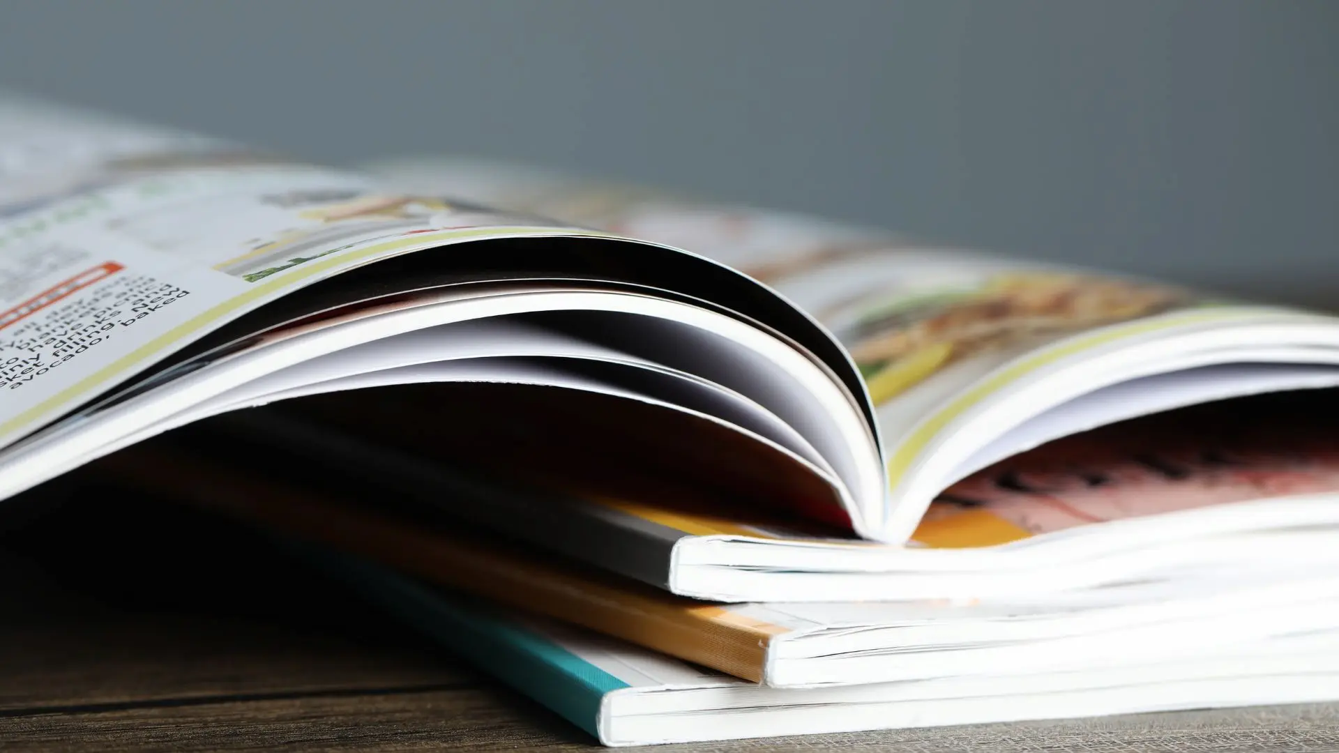 Dettaglio ravvicinato di riviste illustrate aperte e impilate l'una sull'altra sopra una scrivania di legno.