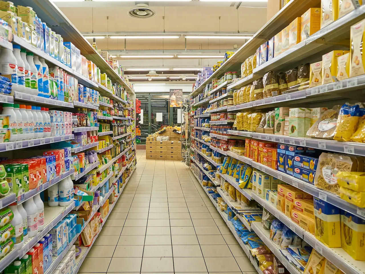 Corsia di un supermercato con scaffali ordinati e pieni di prodotti alimentari. Immagine rappresentativa per un'azienda operante nella Grande Distribuzione Organizzata (GDO).