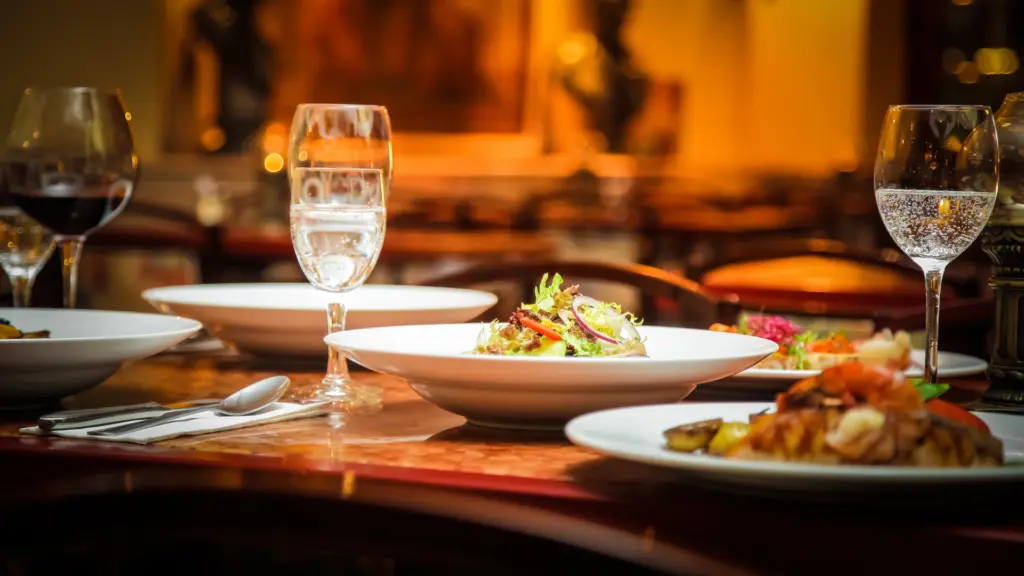 Primo piano di una tavola apparecchiata con piatti di insalata gourmet, calici di vino rosso e acqua in un ambiente accogliente. Immagine rappresentativa di una catena di ristorazione e food retail che ha ottimizzato i costi del personale.