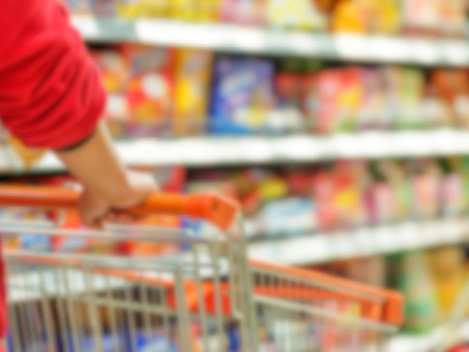 Cliente che spinge un carrello della spesa all'interno della corsia di un supermercato, con scaffali pieni di prodotti sfocati sullo sfondo. Immagine rappresentativa per un'azienda del settore commercio al dettaglio e catene di supermercati.