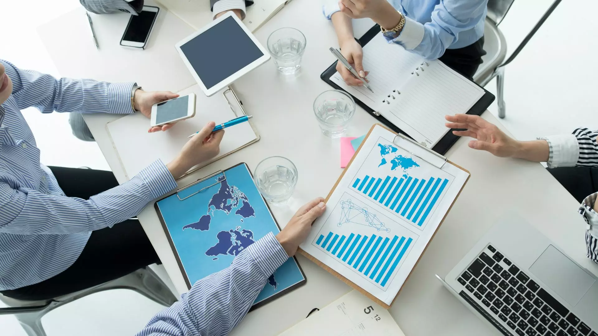 Vista dall'alto di un tavolo da riunione con professionisti che analizzano grafici, dati e planimetrie globali. Immagine rappresentativa di un'azienda di consulenza e servizi IT che ha ottimizzato i propri costi.