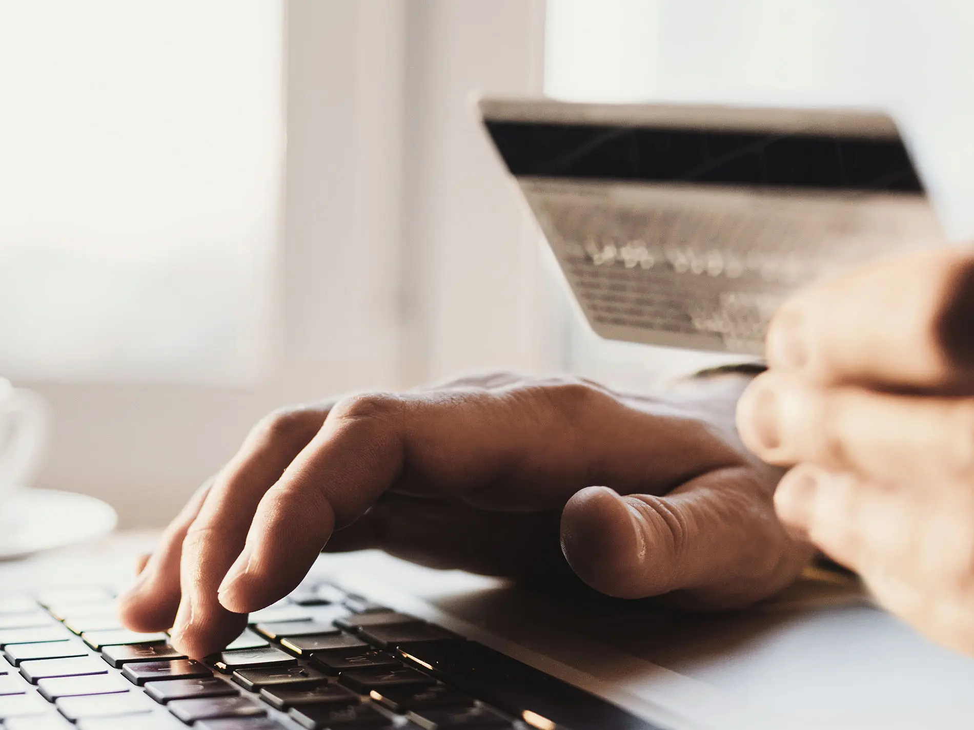 Mani in primo piano che digitano sulla tastiera di un computer portatile mentre tengono una carta di credito. Immagine rappresentativa per il recupero dei contributi nel settore credito.
