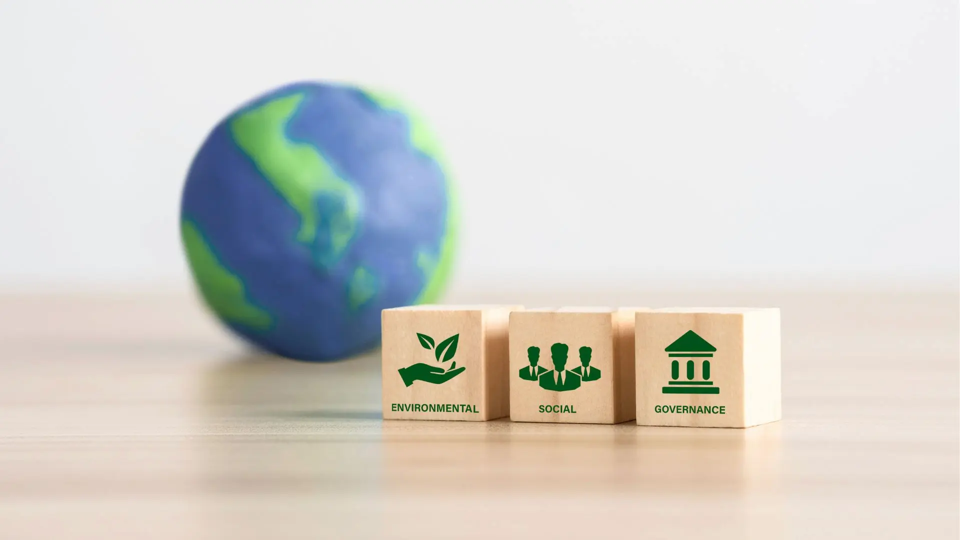 Tre cubi di legno con le parole Environmental, Social e Governance affiancati a un piccolo mappamondo, che rappresentano i pilastri dell'impegno di Fiabilis per la sostenibilità.