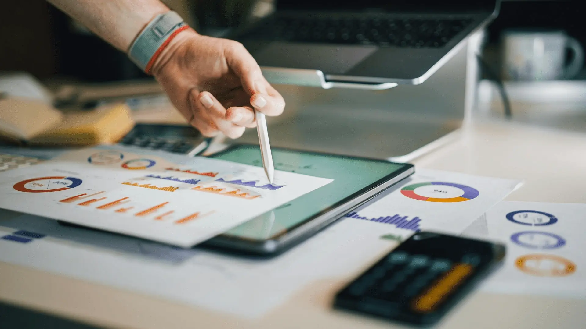Manager analizza con uno stilo grafici e indicatori di performance su tablet e report cartacei, a supporto dell'analisi del costo del lavoro aziendale