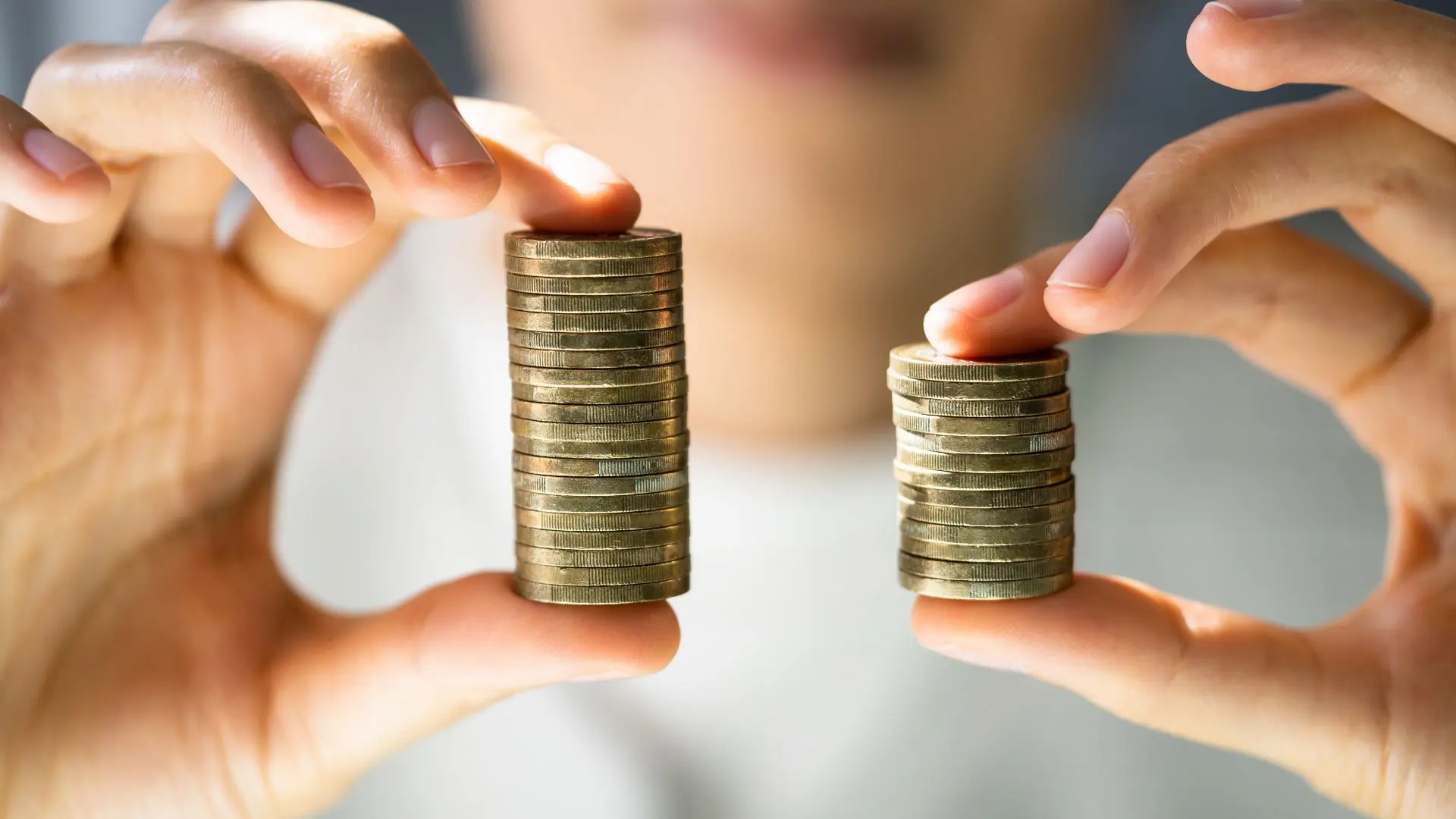 Due mani reggono due pile di monete di altezza diversa, immagine simbolo del divario retributivo di genere che la Direttiva UE 2023/970 sulla pay transparency impone alle aziende di misurare e superare
