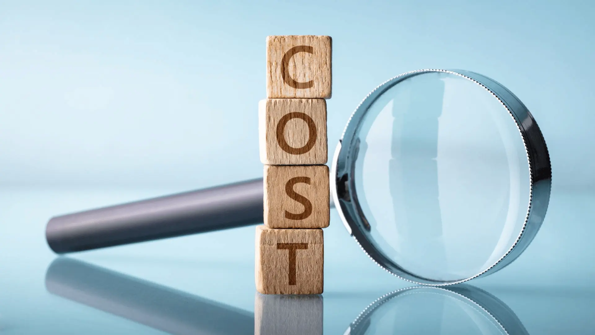 Cubi di legno che compongono la parola COST accanto a una lente d'ingrandimento: l'analisi delle voci dirette e indirette del costo del lavoro in azienda