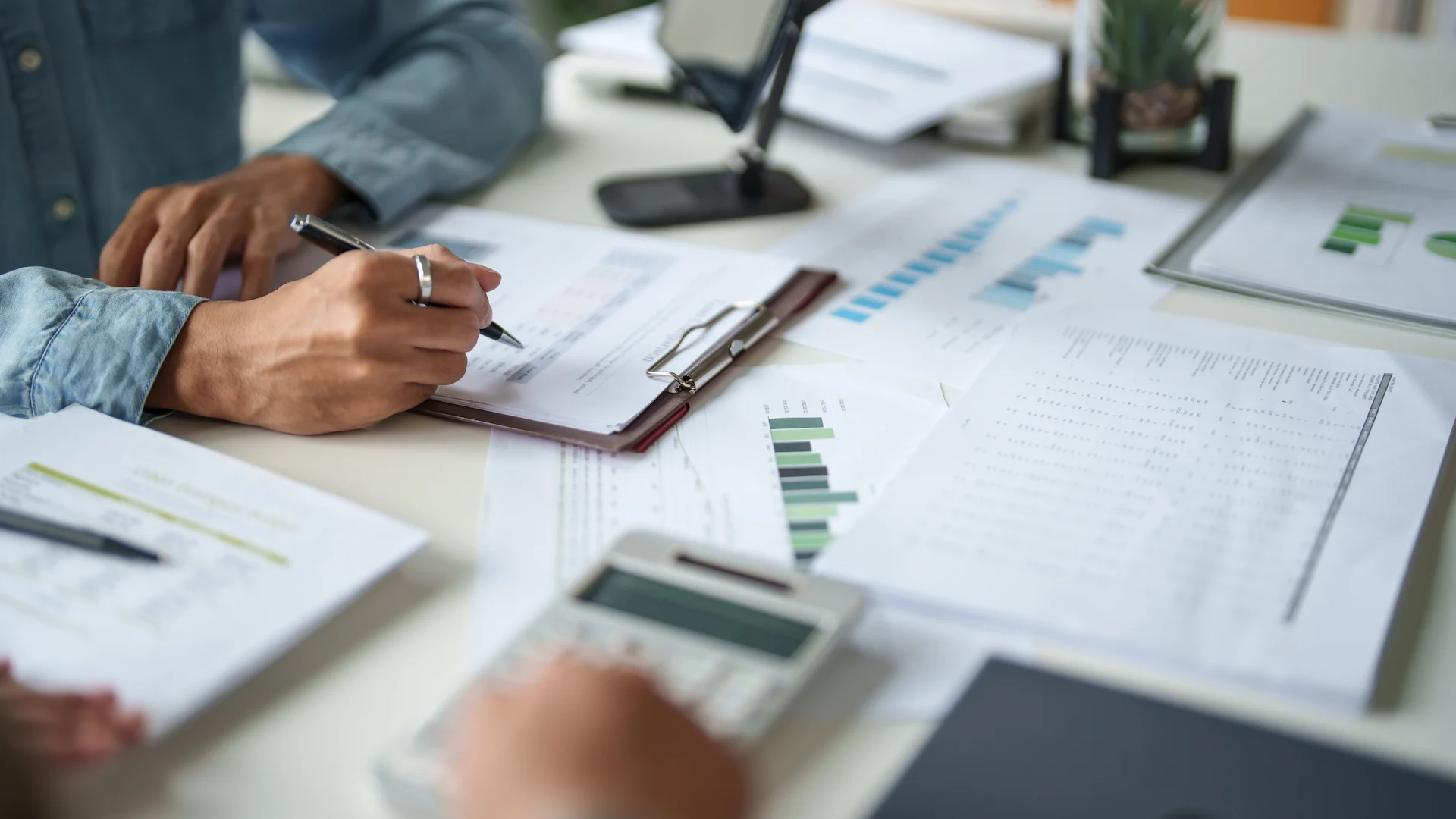 Consulente annota dati su un report finanziario accanto a grafici, prospetti e calcolatrice, durante l'analisi del costo del lavoro aziendale