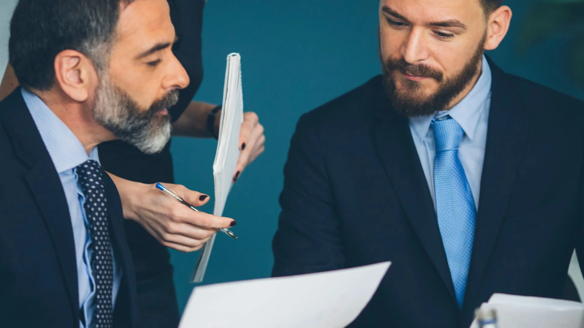 Due professionisti esaminano documenti mentre una collega consegna un fascicolo