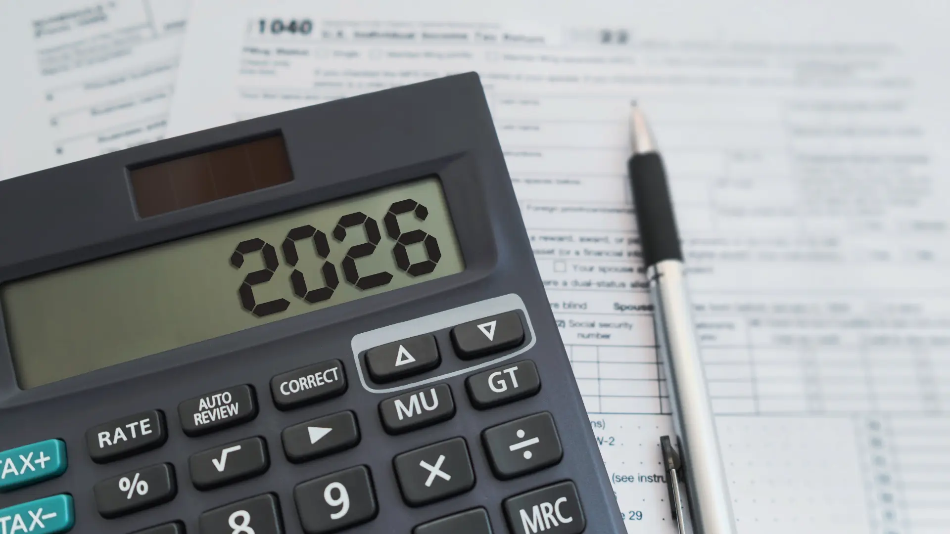 Calcolatrice con il numero 2026 sul display, appoggiata su moduli fiscali accanto a una penna